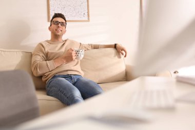 Elinde bir bardak içki olan genç adam B sırasında koltukta dinleniyor.