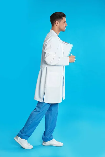 Doctor in uniform met klembord lopen op blauwe achtergrond — Stockfoto