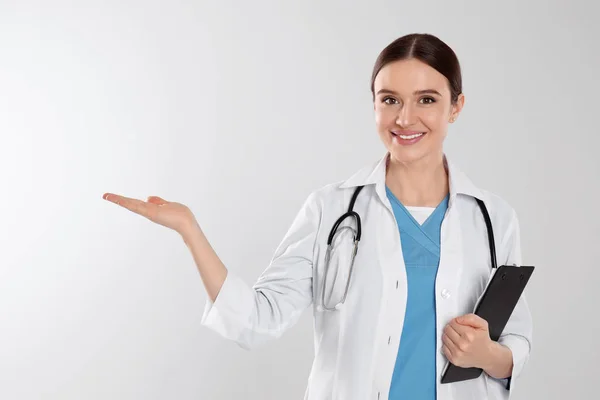 Médico com estetoscópio e área de transferência em fundo cinza claro — Fotografia de Stock