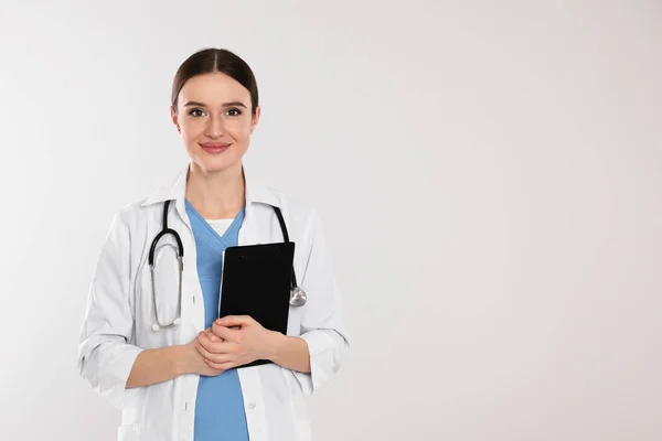 Doctor with stethoscope and clipboard on light grey background. — Stock Photo, Image