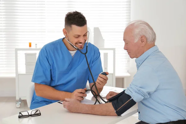 Врач, измеряющий артериальное давление пожилых пациентов в офисе — стоковое фото