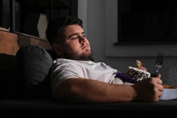 stock image Depressed overweight man eating sweets in living room at night