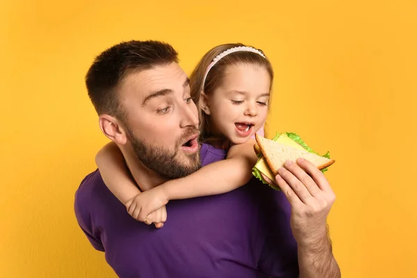Junger Mann und seine Tochter mit Sandwich auf gelbem Hintergrund — Stockfoto
