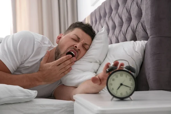 Sleepy man turning off alarm clock at home in morning