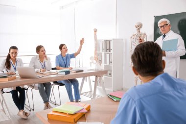 Tıp öğrencileri ve profesör sınıfta insan iskeleti anatomisi okuyor.