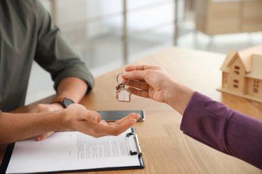 Real estate agent giving key with trinket to client in office, c