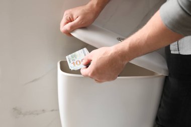 Man hiding money in toilet tank indoors, closeup. Financial savi