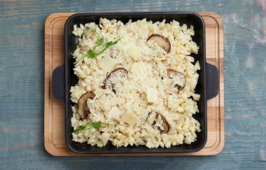 Açık mavi ahşap masada peynirli ve mantarlı leziz risotto.