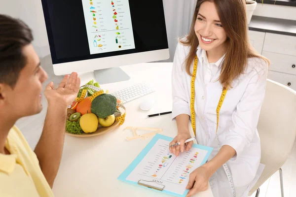 Young nutritionist consulting patient at table in clinic — Stock Photo, Image