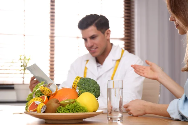 Nutritionist consulting patient at table in clinic, focus on pla — Stock Photo, Image