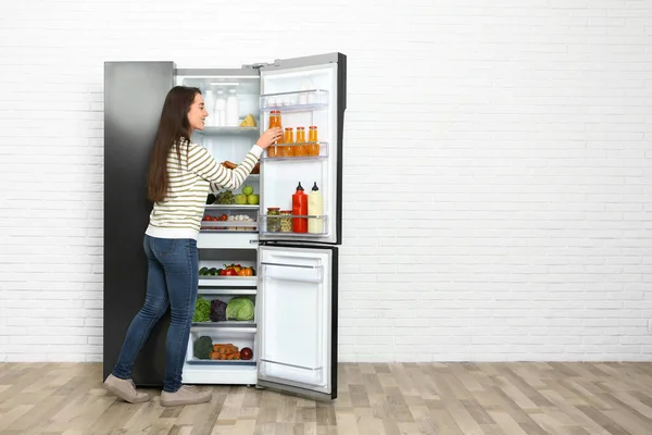 Молодая женщина берет сок из холодильника в помещении, пространство для — стоковое фото