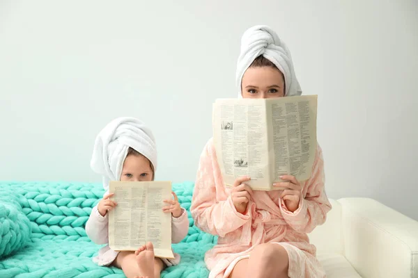 Mother and little daughter in bathrobes with newspapers sitting — 스톡 사진