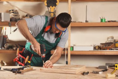 Profesyonel marangoz tezgahta matkapla vida çeviriyor.