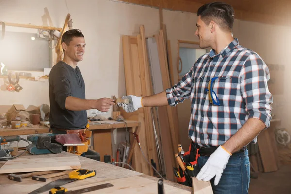 Carpenter giving tool to colleague in workshop — Stock Photo, Image