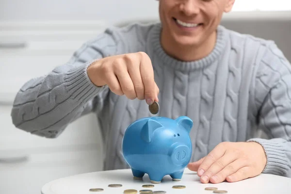 Man zet munt in spaarvarken bank aan witte tafel, close-up — Stockfoto