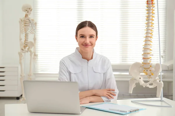 Kobieta ortopeda z laptopem w pobliżu ludzkiego kręgosłupa model w biurze — Zdjęcie stockowe