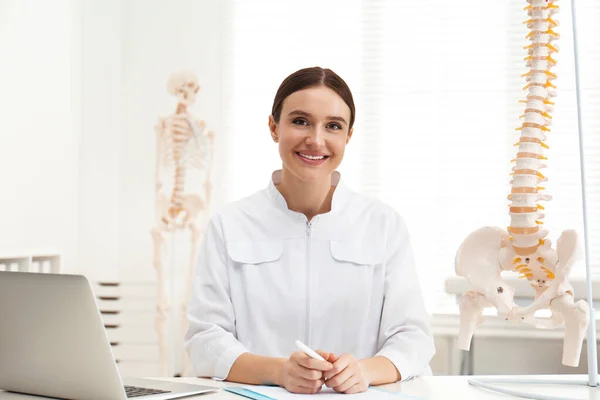 Vrouwelijke orthopeed met laptop nabij menselijk ruggengraat model op kantoor — Stockfoto