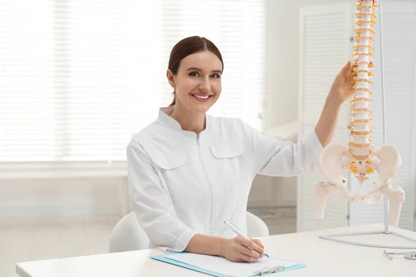 Vrouwelijke orthopeed aan tafel nabij menselijk ruggengraat model in kantoor — Stockfoto