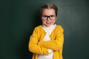 Cute little child wearing glasses near chalkboard. First time at