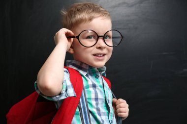 Cute little child wearing glasses near chalkboard. First time at
