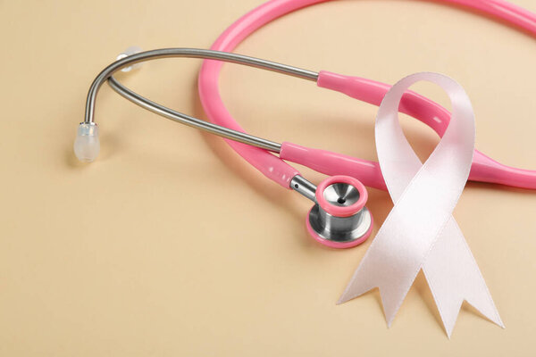 Pink ribbon and stethoscope on beige background, closeup. Breast