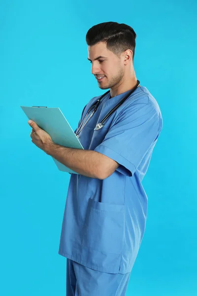 Beau médecin avec presse-papiers sur fond bleu — Photo