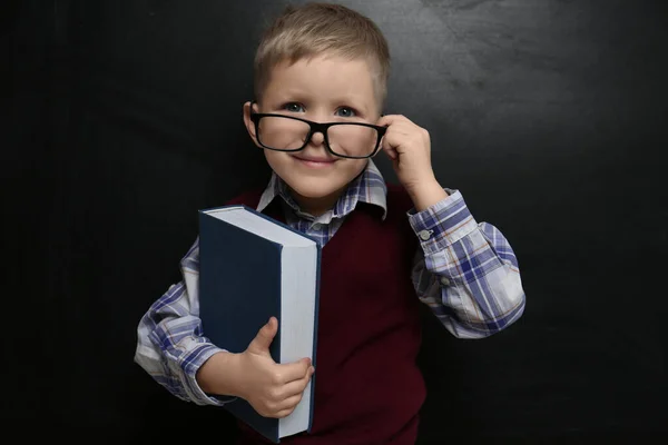 Lindo niño pequeño con gafas cerca de pizarra. Primera vez en — Foto de Stock