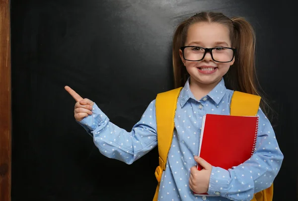 Cute little child wearing glasses near chalkboard. First time at — Stock Photo, Image