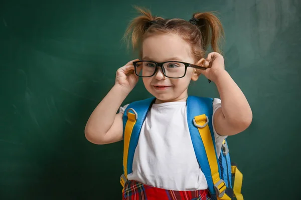 Cute little child wearing glasses near chalkboard. First time at — ストック写真
