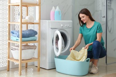 Banyoda çamaşır makinesinin yanında elbiseleri olan genç bir kadın. Laund