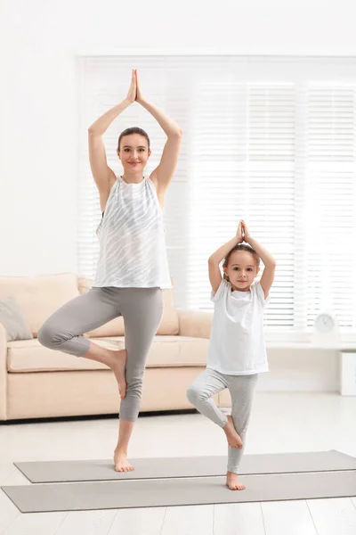 Madre joven con hija pequeña practicando yoga en casa — Foto de Stock