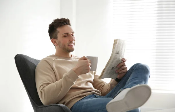 Junger Mann mit Getränk und Zeitung entspannt im Sessel n — Stockfoto