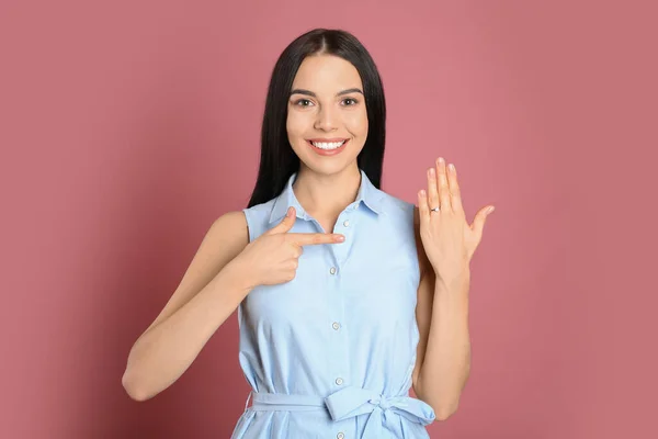 Mujer joven y feliz con un hermoso anillo de compromiso en la espalda rosa — Foto de Stock