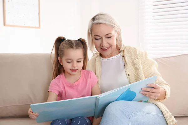 Mature woman with her little granddaughter reading book together — Stock Photo, Image