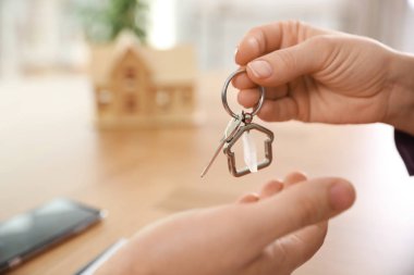 Real estate agent giving key with trinket to client in office, c