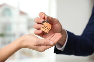 Real estate agent giving key with trinket to client in office, c