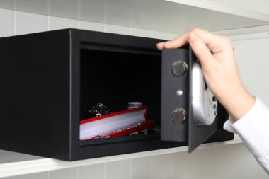 Siyah çelik kasayı açan kadın. Rafta para ve mücevher var. Yakın plan.