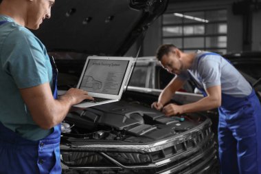 Mechanic with laptop doing car diagnostic at automobile repair s