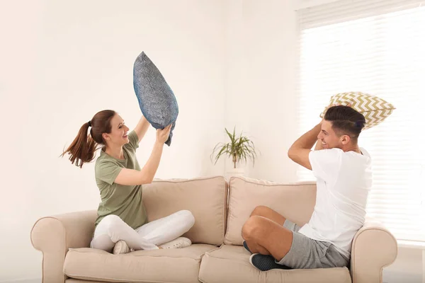 Feliz pareja teniendo pelea de almohadas en la sala de estar —  Fotos de Stock