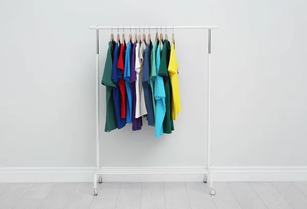 Estante con elegantes camisetas de colores en la habitación —  Fotos de Stock