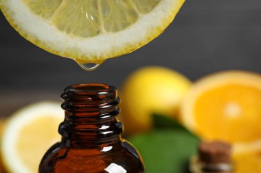 Citrus essential oil dripping from lemon slice into bottle, closeup