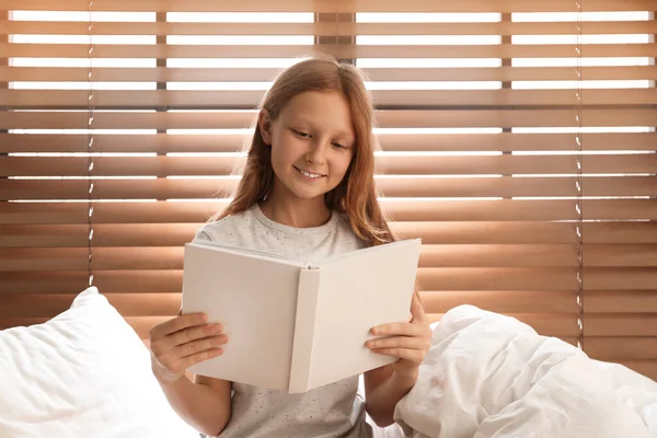 사랑 스러운 십 대 소녀가 창문 근처 침대에서 책을 읽고 있다 — 스톡 사진