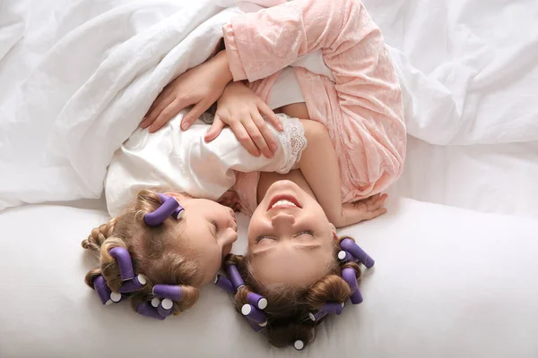 Gelukkig moeder en dochter met krulspelden liggend op bed, bovenaanzicht — Stockfoto