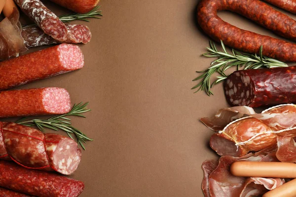 Frame made with different sausages on brown background, flat lay. Space for text