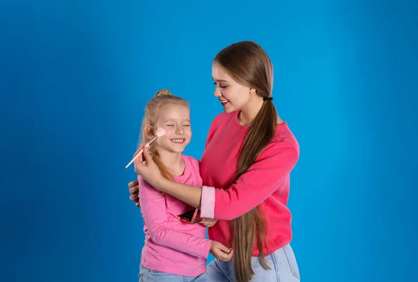 Glückliche Mutter trägt Puder auf das Gesicht ihrer Tochter auf blauem Backgr auf — Stockfoto