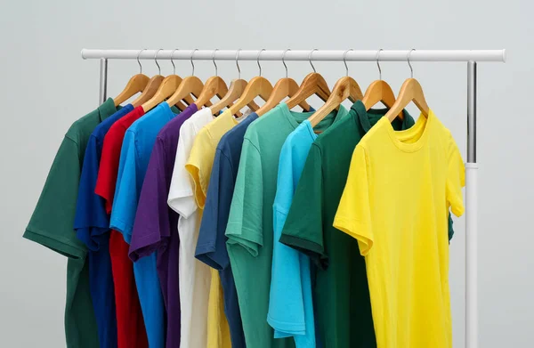 Rack with colorful t-shirts on light background — Stock Photo, Image