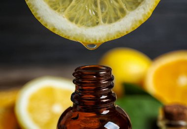 Citrus essential oil dripping from lemon slice into bottle, closeup