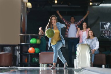 Genç bir kadın top oynuyor ve arkadaşlarıyla bowling kulübünde vakit geçiriyor.