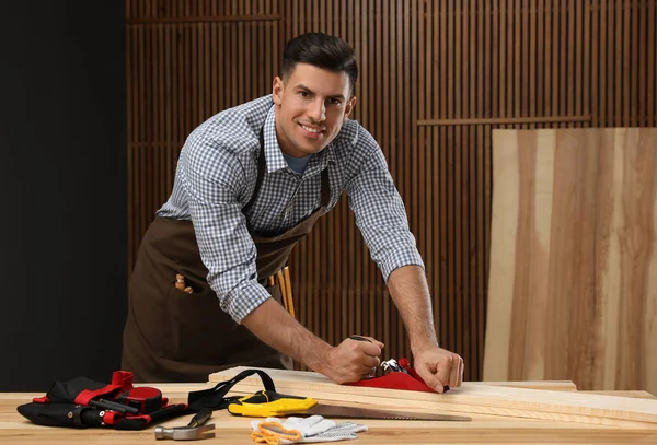 Handsome carpenter working with timber at table indoors
