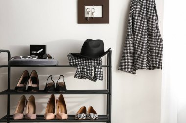 Koridordaki beyaz duvarın yanında siyah raflar, ayakkabılar ve farklı aksesuarlar.